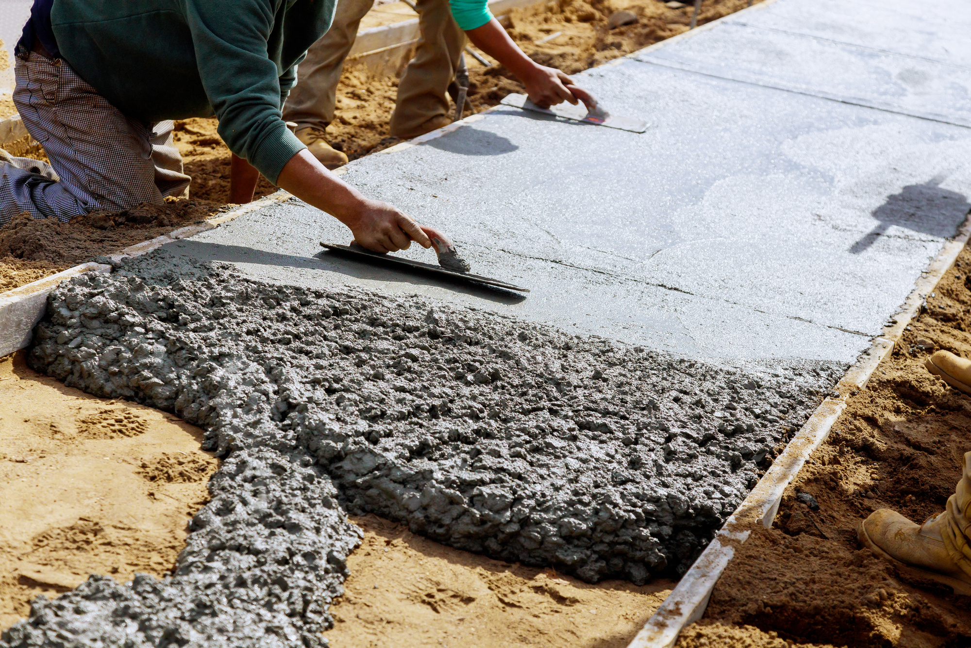 Construction workers laying concrete mixer with concrete mixer on sidewalk